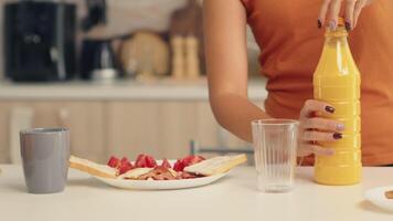 vrouw gieten vers sap in glas voor ontbijt in keuken. vrouw drinken gezond en natuurlijk oranje sap. huisvrouw drinken gezond, natuurlijk, eigengemaakt oranje sap. verfrissend zondag ochtend- video