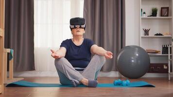 Senior Frau meditieren auf Yoga Matte tragen vr Headset. aktiv gesund Lebensstil sportlich alt Person Ausbildung trainieren Zuhause Wellness und Innen- ausüben video