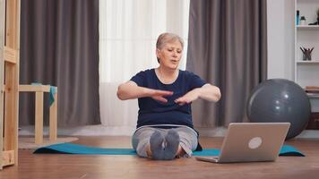 senior kvinna Sammanträde på yoga matta stretching pojke Sammanträde på matta. uppkopplad inlärning och studie, aktiva friska livsstil sportig gammal person Träning träna Hem wellness och inomhus- utövar video