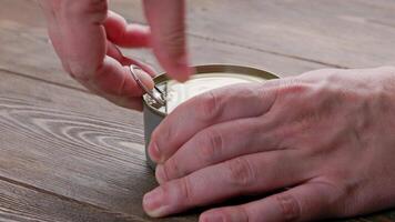 caucasian hands opens tin can with pull ring on wooden surface video