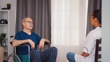 Handicapped senior man in wheelchair having a conversation with nurse. Disabled disability old person with medical worker in nursing care home assistance, healthcare and medicine service video