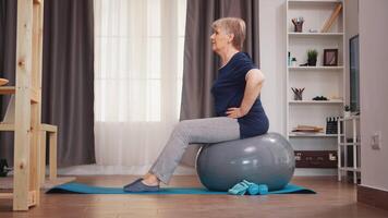 Old woman workout on training ball in living room. Old person training home healthy retirement lifestyle stretching, home training and exercise video