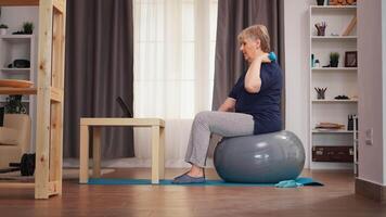 Senior mulher Treinamento bíceps em estabilidade bola assistindo conectados lição. conectados Treinamento Aprendendo tecnologia velho mulher elevação Treinamento saudável estilo de vida esporte ginástica exercite-se às casa com pesos haltere atividade video