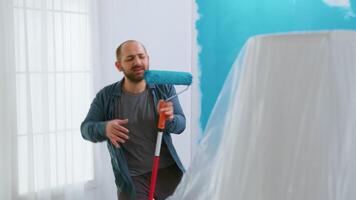 reparar homem cantando em rolo escova com azul pintura durante casa renovação. dançando, construção, reparando, trabalhando. redecoração e casa construção enquanto renovando e melhorando. reparar e decoração. video