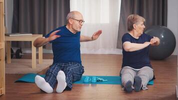 anziano coppia allungamento loro corpi su yoga stuoia nel vivente camera. vecchio persona salutare stile di vita esercizio a casa, allenarsi e addestramento, sport attività a casa video