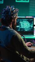 Vertical video Computer engineer trying to make EEG headset work, researching brain machine transferring. Man doing SF online consciousness uploading, trying to transcend out of simulation, camera A