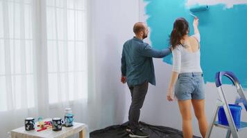 Adults renovating apartment painting wall using roller brush with blue paint. Apartment redecoration and home construction while renovating and improving. Repair and decorating. video