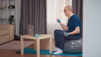 anziano uomo formazione nel vivente camera con manubri durante in linea fitness programma. vecchio persona pensionato salutare formazione assistenza sanitaria sport a casa, esercizio fitness attività a anziano età video