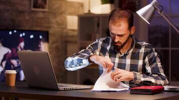 uomo d'affari digitando su il computer portatile e ricerca attraverso documenti mentre Lavorando a partire dal casa ufficio. video