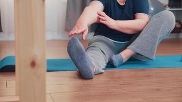 oud vrouw uitrekken zittend Aan yoga mat in leven kamer. oud persoon gepensioneerde oefening opleiding Bij huis sport werkzaamheid Bij ouderen pensioen leeftijd video