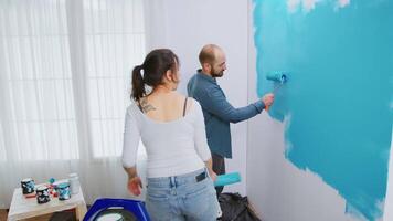 Caucasian married couple doing a makeover of their apartment painting the walls with roller brush. Apartment redecoration and home construction while renovating and improving. Repair and decorating. video