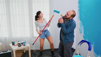 Married couple singing on renovation tools dipped in blue paint. Cheerful married couple during home makeover. Home decoration and renovation in cozy apartment flat, repair and makeover video