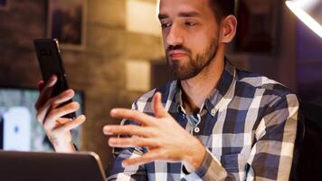 Businessman giving explanations during a video call on mobile phone while working from home office. Entrepreneur working late.