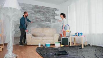 Married couple covering sofa with plastic sheet for home decorating. Apartment redecoration and home construction while renovating and improving. Repair and decorating. video