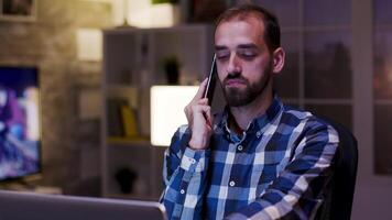 overwerkt zakenman geeuw gedurende een gesprek Aan mobiel telefoon. zakenman werken in huis kantoor gedurende laat uur. video