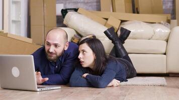 Happy couple sitting on the floor of their new apartment while making online shopping on laptop. Zoom in shot. video