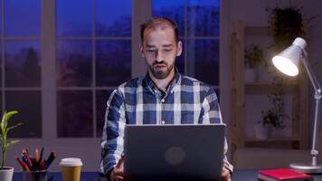 Caucasian entrepreneur talking during a video call on his laptop. Bearded entrepreneur working late in his home office.