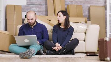Couple smiling while sitting on the floor of their new apartment and doing online shopping using laptop. video