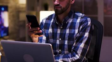 jong zakenman glimlachen terwijl op zoek in zijn mobiel telefoon. zakenman in zijn huis kantoor. video