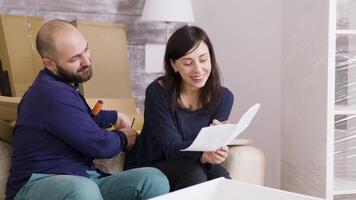 paar glimlachen terwijl in elkaar zetten een plank in hun nieuw appartement. vriendin lezing instructies. vriendje gebruik makend van schroevendraaier. video