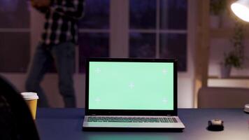 Mock up green screen laptop standing on the desk in home office. Zoom in shot. Businessman in the background. video