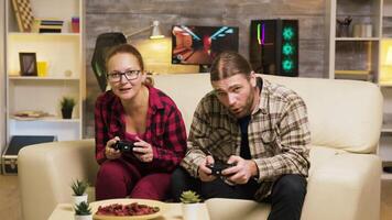 Young couple disappointed after losing at online video games. Using wireless controllers to play video games.