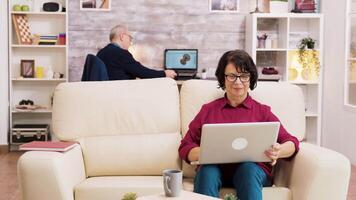 idosos casal durante uma vídeo ligar sentado em a sofá dentro a vivo sala. envelhecido pessoas usando moderno tecnologia video
