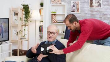 Young man learning old man how to use VR headset in living room. video