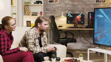 Girlfriend sitting on the couch next to her boyfriend while he's playing video games on tv using wireless controllers.