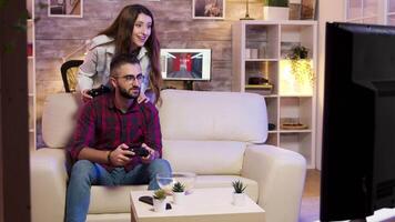 Man playing video games on television using controllers while his girlfriend in cheering in the back.