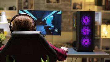 Dolly shot of woman sitting on gaming chair playing computer games. Man lying on sofa in the background. video