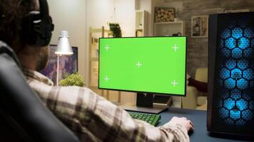 man med hörlurar spelar spel på dator med grön skärm i levande rum. video