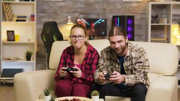 Excited couple giving high five while playing online video games sitting on couch using wireless controllers.