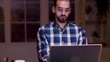 stanco uomo d'affari sbadigli mentre Lavorando su il suo il computer portatile durante notte ore nel il suo casa ufficio. video