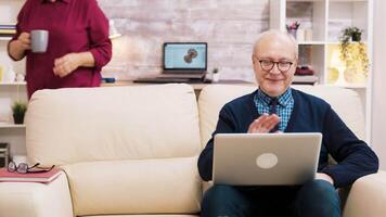 contento mayor medio Envejecido Pareja sentado en sofá ondulación a ordenador portátil durante un vídeo llamar. video