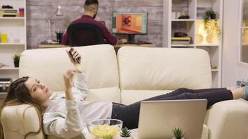 schön jung Mädchen Lügen auf das Couch mit ihr Telefon. Freund im das Hintergrund. video