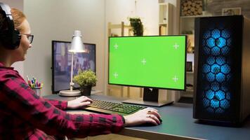 vrouw met hoofdtelefoons spelen spellen Aan groen scherm computer in leven kamer. vrouw zittend Aan gaming stoel. video