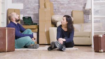 Couple sitting on carpet in their new apartment with suitcases in front of them. Cardboard boxes in the background. video