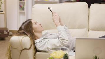 Pretty girl relaxing on the couch using her smartphone. Boyfriend in the background. video