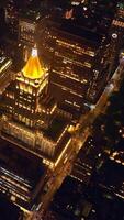 New York Life Building with shining golden roof at night. Beautifully-lit structure standing out at the backdrop of other architecture. Top view. Vertical video