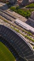 Empty Soldier Field Stadium neighboring busy highway and railway depot. Numerous green zones of the area. Sunny day backdrop. Top view. Vertical video