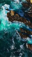 Amazing sight of mesmerizing waves splashing by the rocks. Azure water with foamy tide arriving to the coast of California. Vertical video
