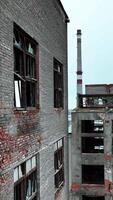 Old brick and concrete premises of an abandoned factory. Huge industrial territory with ruined constructions at the backdrop of a city. Vertical video