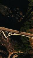 Straße auf das Brücke Über das Spalt zwischen das Berge. absteigend über das schön Brücke Konstruktion auf sonnig Tag. Aussicht von oben. Vertikale Video