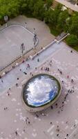 People walking around famous Cloud Gate sculpture in Chicago. The Bean reflecting sky, clouds, park and skyscrapers in its top surface. Top view. Vertical video