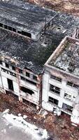 Large buildings of an old abandoned factory not used for a very long time. Forlorn empty premises with no windows or parts of the walls. Aerial view. Vertical video