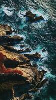 hermosa blanco olas salpicaduras por el rocas a el costa de California. escabroso apuntalar de el Pacífico Oceano desde aéreo perspectiva. vertical vídeo video