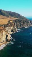 Pacífico Oceano salpicaduras olas por el escarpado acantilado rocas increíble paisaje de carreteras a través de el hermosa montañas. azul cielo a fondo. vertical vídeo video