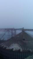 Metal supports connecting the tops of huge silo tanks. Powerful granary reservoirs in foggy winter weather. Top view. Vertical video