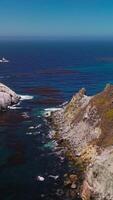 Scharf stachelig Felsen mit etwas Flechte wachsend An. schön Landschaft von das Blau Meer Wasser mit Algen auf Oberfläche. dunstig Horizont beim Hintergrund. Vertikale Video